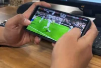 Seorang pemain memainkan game FC Mobile EA Sports melalui ponsel saat pertandingan virtual berlangsung.