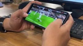 Seorang pemain memainkan game FC Mobile EA Sports melalui ponsel saat pertandingan virtual berlangsung.