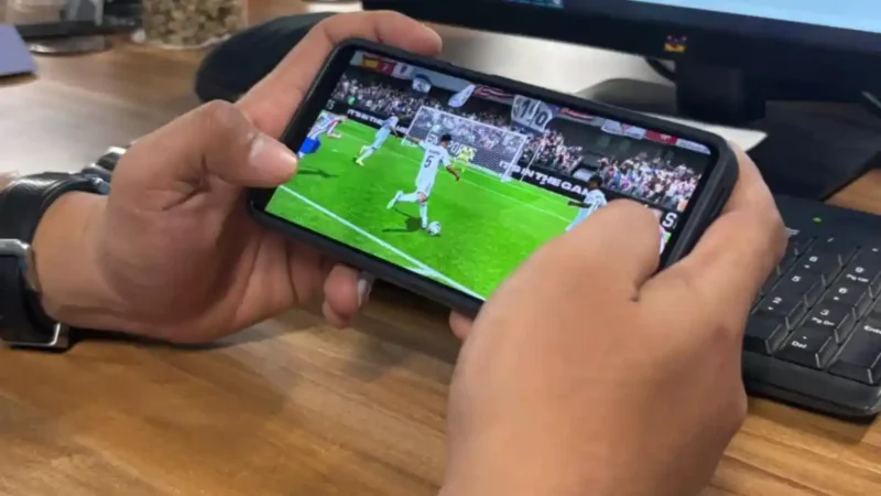 Seorang pemain memainkan game FC Mobile EA Sports melalui ponsel saat pertandingan virtual berlangsung.