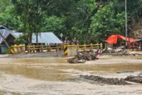 Luapan Sungai Batang di Palembayan, Agam, menutup akses jalan setelah hujan deras. Kayu gelondongan tampak tersangkut di jembatan, membuat arus semakin deras.
