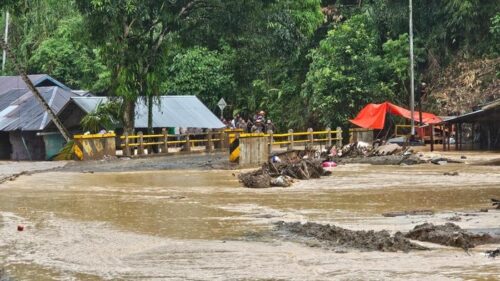 Luapan Sungai Batang di Palembayan, Agam, menutup akses jalan setelah hujan deras. Kayu gelondongan tampak tersangkut di jembatan, membuat arus semakin deras.
