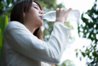 Seorang perempuan meminum air putih dari botol sebagai upaya memenuhi kebutuhan cairan tubuh.