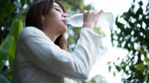 Seorang perempuan meminum air putih dari botol sebagai upaya memenuhi kebutuhan cairan tubuh.