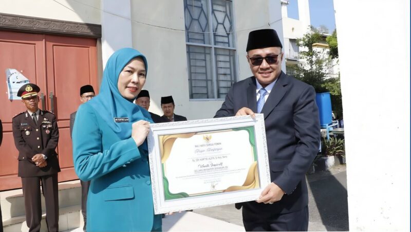 Wali Kota Sungai Penuh, Alfin, menyerahkan penghargaan kepada Ketua TP PKK Sri Kartini Alfin sebagai penggagas Gerakan 3S dalam apel Hari Kebangkitan Nasional 2026.